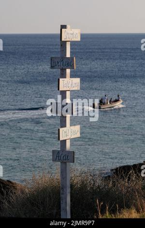 Blick auf hölzerne Schilder für Take Away, Live-Musik, acai, kaltes Gebräu, vegan, Smoothies und das Meer im Hintergrund am Strand von Mylopotas iOS Greece Stockfoto