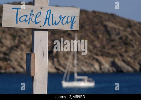 Blick auf hölzerne Schilder für Take Away und Live-Musik und das Meer im Hintergrund am Strand von Mylopotas in iOS Griechenland Stockfoto