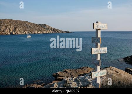 Blick auf hölzerne Schilder für Take Away, Live-Musik, acai, kaltes Gebräu, vegan, Smoothies und das Meer im Hintergrund am Strand von Mylopotas iOS Greece Stockfoto