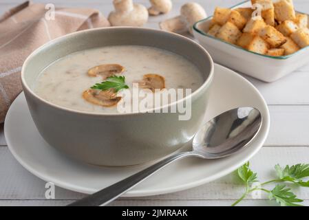 Pilzsuppe in einer grauen Schüssel auf einem hölzernen Hintergrund. Stockfoto