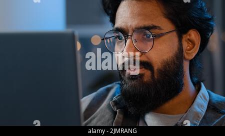 Nahaufnahme des bärtigen männlichen Gesichts Reflexionslicht vom Laptop-Monitor in der Brille. Beschäftigt ernst fokussierten arabischen indischen Mann Blick auf Computer arbeiten freiberuflich Stockfoto