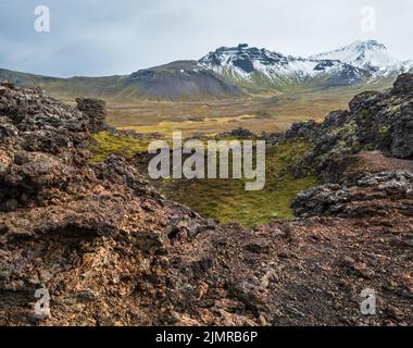 Spektakuläre vulkanische Aussicht vom Saxholl Krater, Snaefellsnes Halbinsel, West Island. Der schneebedeckte Vulkan Snaefellsjokull ist weit oben. Stockfoto