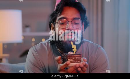 Porträt araber glücklich indischen männlichen Gesicht bärtigen Mann trägt festlichen Geburtstag rosa Hut und Brille hält Cupcake macht Wunsch freudig gratuliert zu Hause Stockfoto