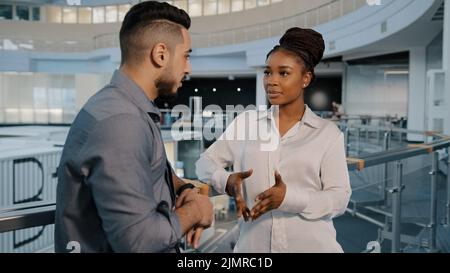 Afroamerikanische Frau und arabisch-indischer Geschäftsmann im Gespräch in Loft-Bürohalle Arbeitspause diverse Kollegen diskutieren Nachrichtenprojekt in lockerer c Stockfoto