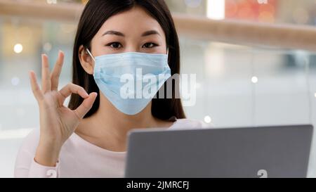 Asiatische ethnische Dame Porträt koreanisch erfolgreiche zufriedene Geschäftsfrau freiberuflich Student Spezialist mit Laptop trägt Gesicht medizinische Maske Blick auf Stockfoto