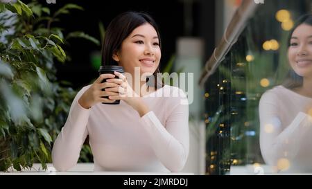 Asiatische Mädchen Frau lächelnd genießen trinken duftenden leckeren Kaffee heißen Tee Morgen Cappuccino im Café am Tisch sitzen lächelnd warten auf Treffen Stockfoto