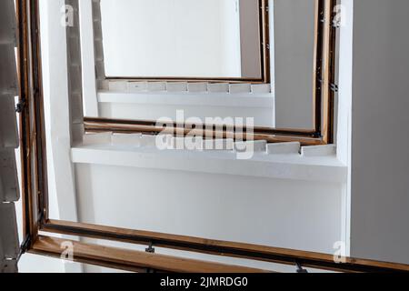 Weiße Steintreppe mit Holzgeländer an einer weißen Decke. Ansicht von unten Stockfoto