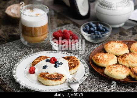 Hüttenkäse-Pfannkuchen zum Frühstück mit Heidelbeeren und Himbeeren und saurer Rahm. Stockfoto