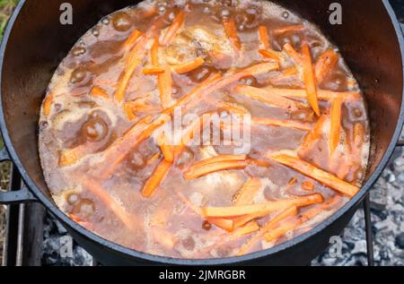 In Scheiben geschnittene orangefarbene Karotten, die in einer Brühe in einem Kessel schmoren Stockfoto