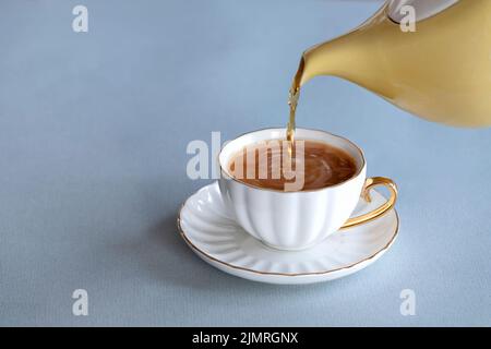 Ein frisches Teegebräu, das aus einer traditionellen englischen teekanne in eine Tasse aus knochenporzellan auf einer Untertasse gegossen wird. Es ist ein starkes Gebräu mit etwas Milch Stockfoto