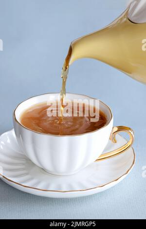 Ein frisches Teegebräu, das aus einer traditionellen englischen teekanne in eine Tasse aus knochenporzellan auf einer Untertasse gegossen wird. Es ist ein starkes Gebräu mit etwas Milch Stockfoto