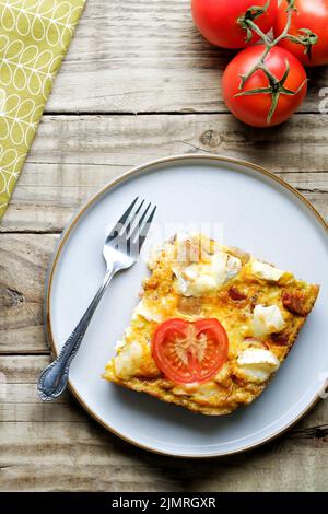 Ein Stück frisch zubereiteter Ziegenkäse-Frittata. Eine Option für gesunde Ernährung auf Ei-Basis. Die Frittata ist beschichtet und liegt auf einem Holztisch auf Stockfoto