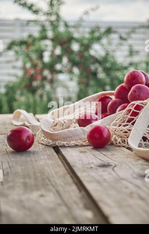 Saftige Pflaumen in umweltfreundlichem Öko-Netzbeutel mit Schnur auf Holzhintergrund Stockfoto