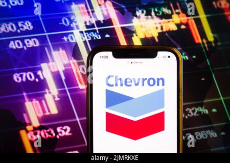 KONSKIE, POLEN - 07. August 2022: Smartphone mit Logo der Chevron Corporation auf dem Hintergrund des Börsendiagramms Stockfoto