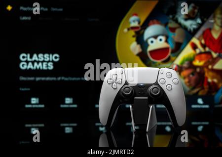 7. August 2022, Odessa, Ukraine. Weißes neues PlayStation 5-Gamepad mit PlayStation Plus auf dem Bildschirm, selektiver Fokus. Klassische Spiele. Dunkler Hintergrund. Stockfoto