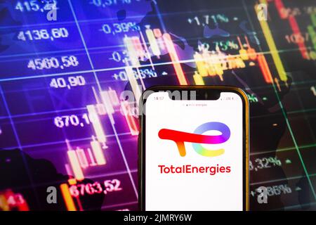 KONSKIE, POLEN - 07. August 2022: Smartphone mit Logo der Gesellschaft TotalEnergies SE im Hintergrund des Börsendiagramms Stockfoto