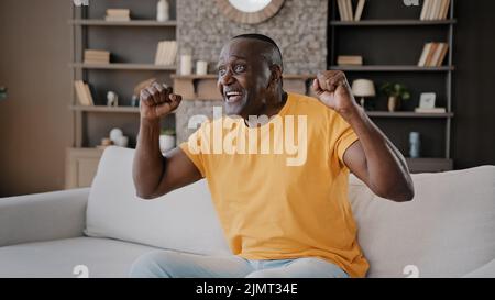Senior-Fußball-Fan afroamerikanischen Mann Bachelor sitzen auf gemütlichen Sofa in der Wohnung beobachten TV Sport-Programm Hockey-Meisterschaft Verwurzelung für Lieblings-Team Stockfoto
