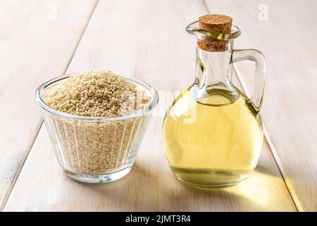Frisches Sesamöl in einem Glaskrug und Schale mit rohen Samen auf einem Holztisch. Sesamum indicum für die Ölproduktion. White til für gesunde Ernährung. Stockfoto