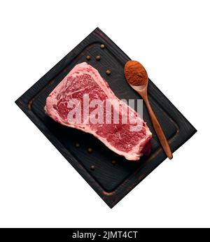 Rohes saftiges Stück Rindfleisch auf dem Knochen liegt auf einem Holzschneidebrett, Gewürze zum Kochen auf schwarzem Hintergrund. Fleisch-Tenderlo Stockfoto