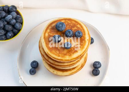 Stapel von leckeren Pfannkuchen auf weißem Teller mit frischen Heidelbeeren auf und in einer Schüssel. Draufsicht, Kopierbereich Stockfoto