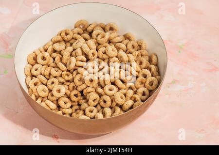 Köstliche Honig Cheéroios Müsli in einer Schüssel auf rosa Hintergrund. Nahaufnahme, flach liegend, Kopierbereich. Frühstückskonzept Stockfoto