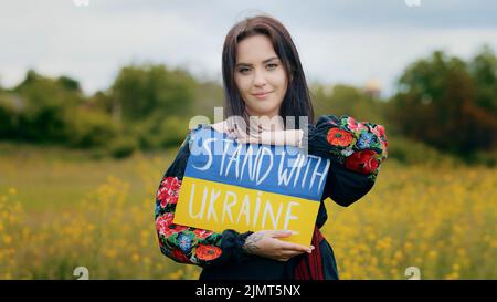 Stilvolle kaukasische Mädchen Frau Aktivistin trägt patriotische nationale ukrainische Kleid junge hübsche Dame mit demonstrierenden Pappe Zeichnung blau gelb Stockfoto