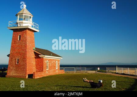 Eine junge Frau trainiert auf dem Rasen vor dem Abbott Memorial Lighthouse, bevor sie in der Nähe von Santa Cruz, Kalifornien, im Ozean surft Stockfoto