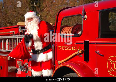 Der Weihnachtsmann kommt bei einem Weihnachtsfest an und wird von einem großen roten Feuerwehrauto transportiert Stockfoto