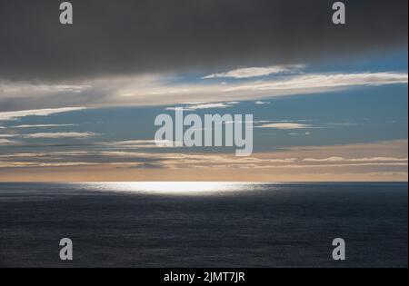 Abendsonne blendet über dem Wasser der Atlantikküste mit leuchtendem Sonnenblend auf der Meeresoberfläche und dem Sonnenuntergangshimmel. Stockfoto