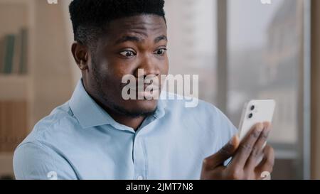 Afrikanischer Mann überrascht erstaunt Millennial 30s Mann Arbeiter sprechen Remote auf Handy schöner amerikanischer Erwachsener Kerl machen Videoanruf schockiert durch plötzliche p Stockfoto