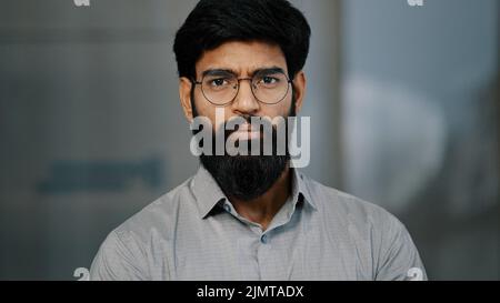 Porträt eines seriös schönen arabischen jungen männlichen bärtigen Mannes in einer Brille tragen Hemdstände, die drinnen posieren und unglücklich in der Nahaufnahme der Kamera stehen Stockfoto