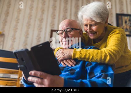 Glückliches kaukasisches Seniorenpaar, das lächelt und umarmt, während es mit ihren Kindern im facetime-Videochat über ein neues Smartphone spricht. Hochwertige Fotos Stockfoto