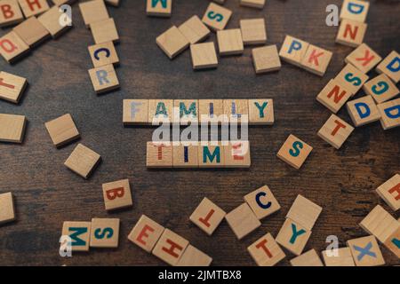 Frohe Spielnacht. Konzept für Freizeitaktivitäten. Bunte quadratische Holzbuchstaben auf einem dunklen Holztisch, die die Worte FAMILIENZEIT schaffen. Hochwertige Fotos Stockfoto