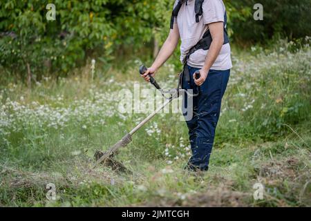 Junge kaukasische Mann Landwirt Gärtner auf dem Feld mit Saitenschneider Benzin Bürstenschneider Schnitt Unkrautgras arbeiten auf dem Bauernhof schneiden auf dem Feld i Stockfoto