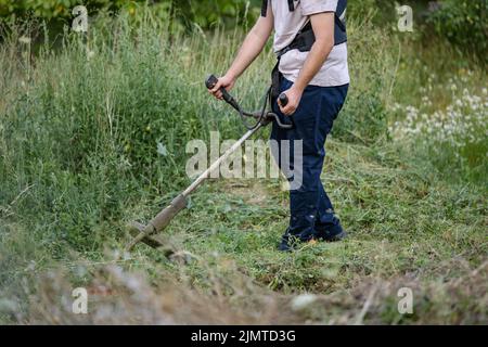 Junge kaukasische Mann Landwirt Gärtner auf dem Feld mit Saitenschneider Benzin Bürstenschneider Schnitt Unkrautgras arbeiten auf dem Bauernhof schneiden auf dem Feld i Stockfoto