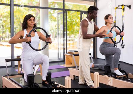 Gesundheitsfachkraft hilft einem Mann, die Gesundheit mit Gymnastikring in Pilates-Klasse wiederherzustellen Stockfoto