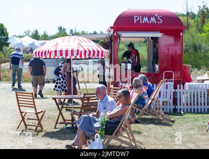 Besucher entspannen sich auf Liegestühlen in der Nähe des Pimms-Standes in der RHS Hyde Hall Flower Show. RHS Hyde Hall Gardens, Chelmsford, Essex, Großbritannien. August 2022 Stockfoto