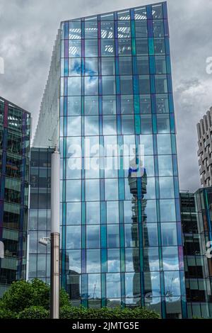 London, Großbritannien - 3. Juli 2022: Hoher, schlanker BT-Turm, der sich in der bläulichen Glasfassade des Bürogebäudes Regent's Place widerspiegelt. Grünes Laub an der Bott Stockfoto