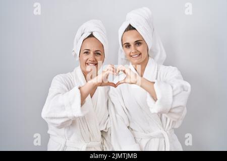 Frau und Tochter mittleren Alters tragen weißen Bademantel und Handtuch lächelnd in der Liebe tun Herz Symbol-Form mit Händen. Romantisches Konzept. Stockfoto
