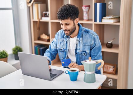 Junger arabischer Mann mit Laptop und Kreditkarte, der zu Hause auf dem Tisch sitzt Stockfoto
