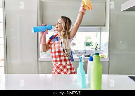 Junge Putzfrau singt mit Waschmittelflasche als Mikrophon in der Küche Stockfoto