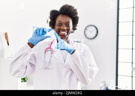 Afrikanische Ärztin, die Spritze in der medizinischen Klinik hält, lächelt glücklich und zeigt mit Hand und Finger Stockfoto