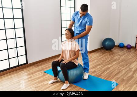 Lateinischer Mann und Frau tragen Physiotherapeutenuniform mit fitem Ball massierenden Hals im Reha-Zentrum Stockfoto
