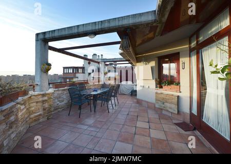 Penthouse-Erkerfenster mit Fliesenboden und Esstisch aus Glas mit grünen Metallstühlen Stockfoto