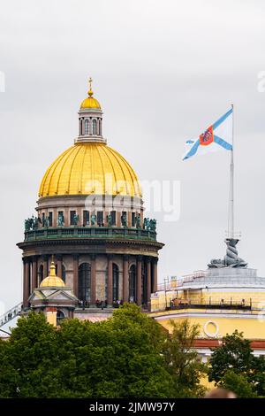 Die riesige goldene Kuppel der Isaakskathedrale und des Admiralität-Gebäudes mit Flagge am Ufer des Flusses Neva in St. Petersburg bei bewölktem Wetter Stockfoto