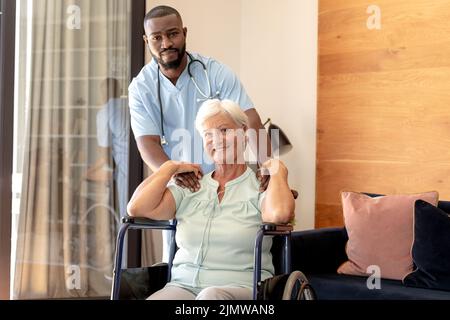 Porträt eines afroamerikanischen männlichen Gesundheitsarbeiters und einer kaukasischen älteren Frau im Rollstuhl zu Hause Stockfoto
