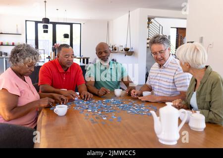 Multirassische ältere Freunde mit Kaffeetassen auf dem Tisch lösen Puzzle im Pflegeheim Stockfoto