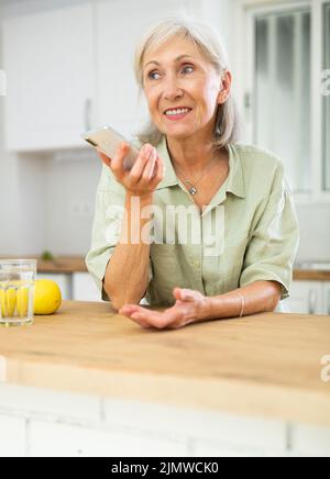 Ältere Frau, die in der Wohnung telefoniert Stockfoto