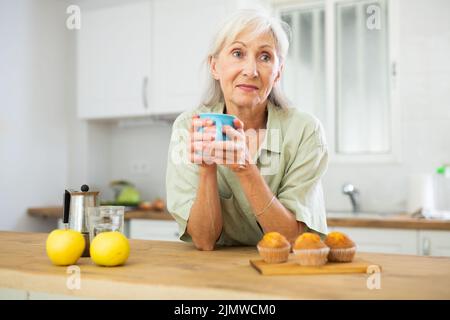 Entspannte ältere Frau, die Kaffee in der Küche trinkt Stockfoto