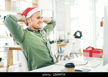 Ein junger Geschäftsmann, der am Heiligabend in seinem Büro arbeitet, entspannt sich mit den Händen hinter dem Kopf. Stockfoto